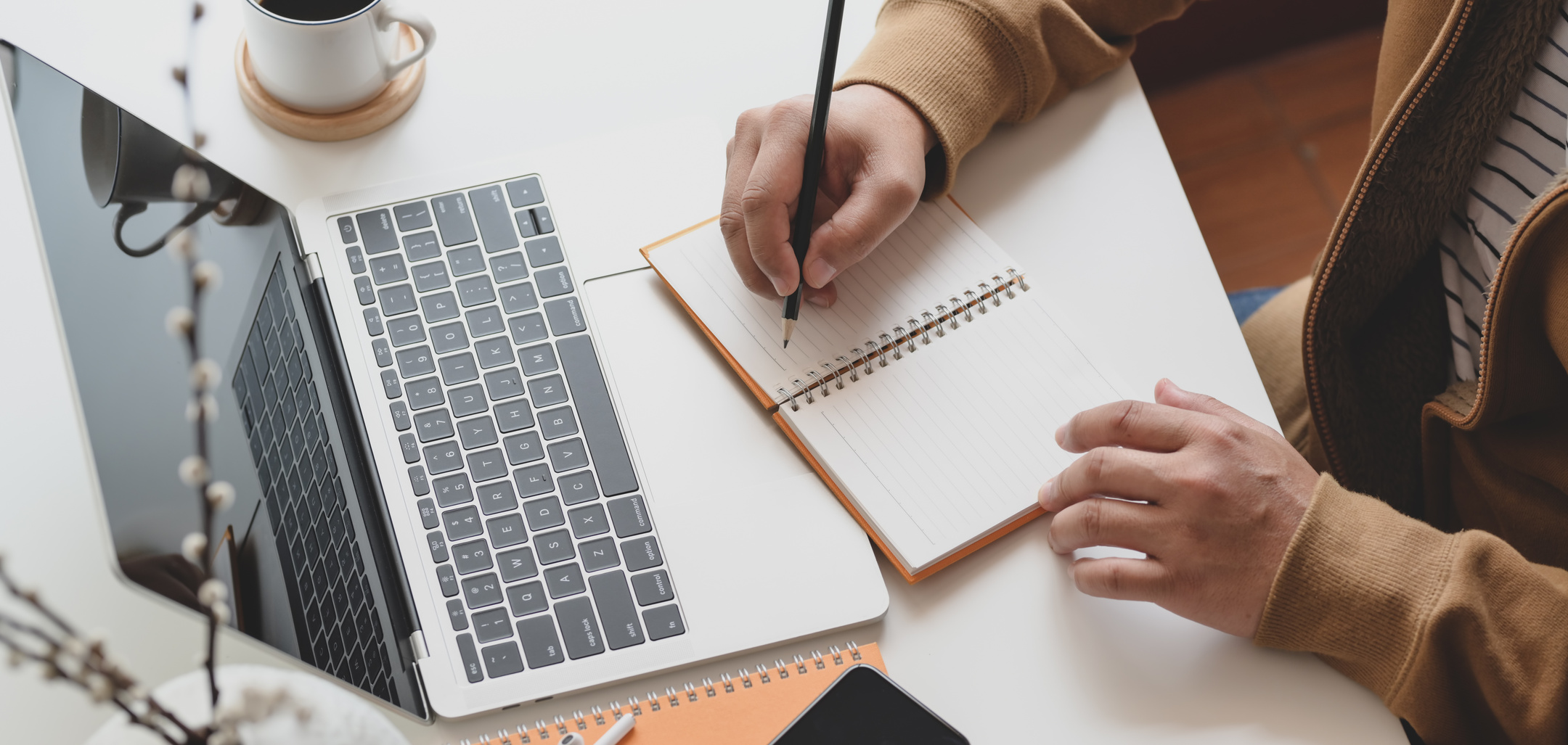 Person Writing on Notebook next to Laptop